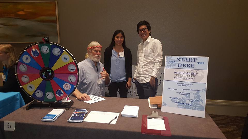 three people at a booth next to a spin wheel and a PBTRC poster