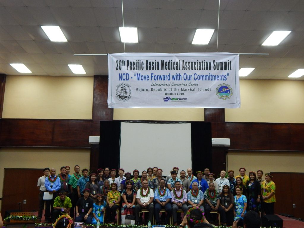 Group of people in chairs on stage under banner
