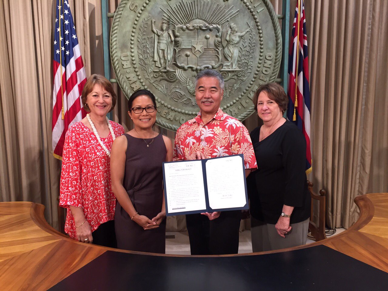 Group of 3 women posing with Governor Ige who is holding up a signed bill