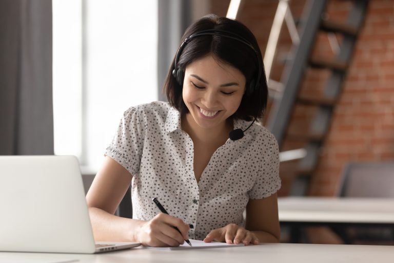Woman in headset writing on paper with a pen