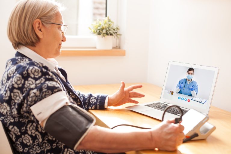 Woman taking blood pressure while talking to doctor on computer